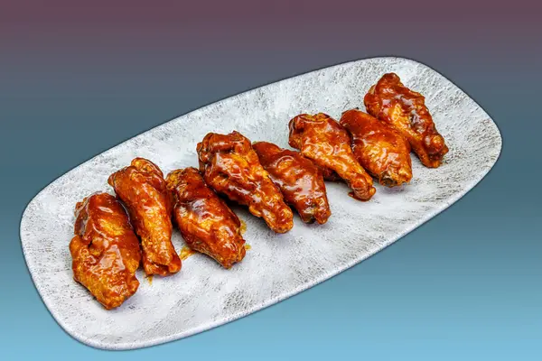 Composition of a plate of chicken wings with barbecue sauce on a magenta and light blue gradient background