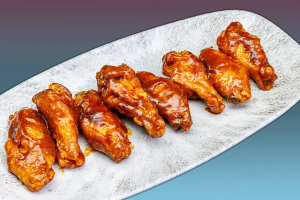 Composition of a plate of chicken wings with barbecue sauce on a magenta and light blue gradient background