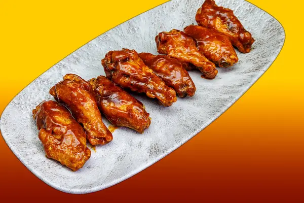 Composition of a plate of chicken wings with BBQ sauce on a yellow and red gradient background