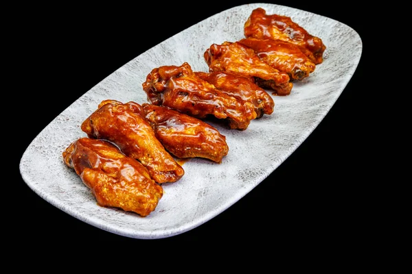 Composition of a plate of chicken wings with barbecue sauce on black background