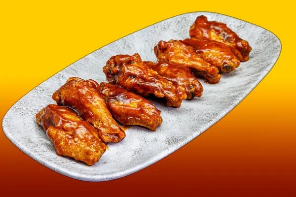 Composition of a plate of chicken wings with BBQ sauce on a yellow and red gradient background
