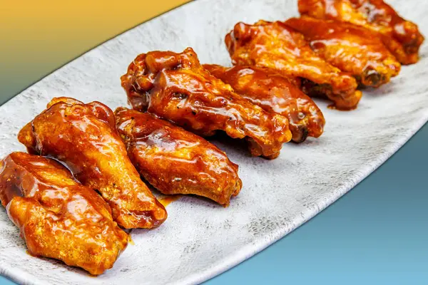 Composition of a plate of chicken wings with BBQ sauce on a yellow and light blue gradient background