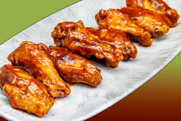 Composition of a plate of chicken wings with BBQ sauce on a green and red gradient background