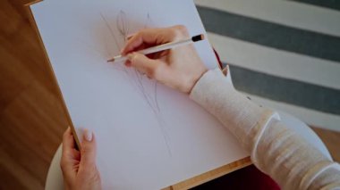 Elinde kalem tutan bir kadın beyaz kağıda çiçek desenleri çiziyor..