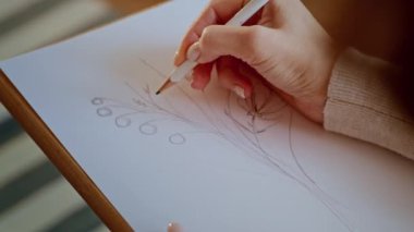 Elinde kalem tutan bir kadın beyaz kağıda çiçek desenleri çiziyor..