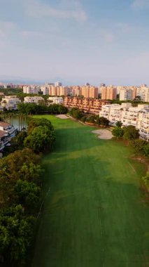 İspanya 'nın Alicante kentindeki yerleşim yerlerine ve şehir binalarına uzanan yemyeşil bir golf sahasının panoramik insansız hava aracı görüntüsü. Fotoğraf yeşil spor sahalarıyla şehir gelişimi arasındaki uyumu vurguluyor..