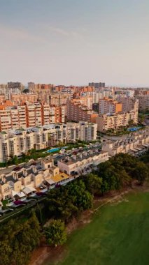 İspanya 'nın Alicante kentindeki San Juan bölgesinde modern apartmanlar, konutlar ve yemyeşil alanlar var. Günbatımı gökyüzüne karşı turuncu ve beyaz mimarinin karşıtlığı sıcak, sinematik bir şehir manzarası yaratır..