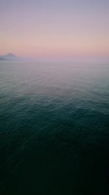 İspanya 'nın Alicante kenti yakınlarındaki Akdeniz üzerinde barışçıl bir insansız hava aracı uçuşu, yumuşak günbatımı ışığı altında kıyı şeridini, kumlu sahili ve şehrin ufuk çizgisini ortaya çıkarmak için yavaşça geçiş yapıyor. Görüntü doğal dokuyu yakalar.