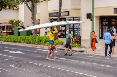 Honolulu, Hawaii - December 28, 2022: Surfer carrying a surfoard across  on Kalakaua Avenue.