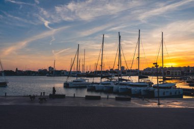 Valencia limanındaki deniz suyuna yansıyan yatlar. İskele vinçleri ufukta. İspanya 'da sıcak bir akşam.