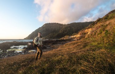 Happy tourist man walk and hike on ocean trail near mountains at sunset time