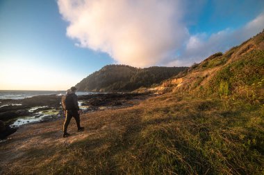 Tourist man walk and hike on ocean trail near mountains at sunset time