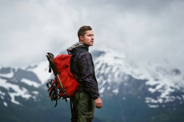 Sırt çantası ve teçhizatıyla dağın tepesine tırmanmaya hazır genç bir adam.