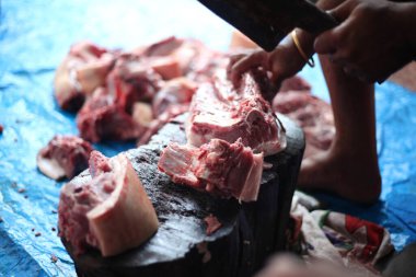 Kasap mezbahada bıçakla çiğ et kesiyor.