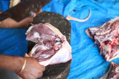 Kasap mezbahada bıçakla çiğ et kesiyor.