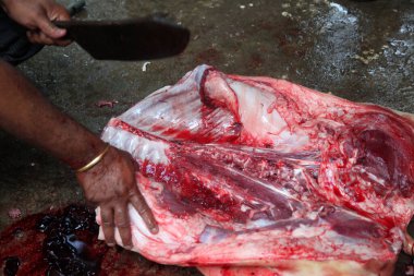 Kasap mezbahada bıçakla çiğ et kesiyor.