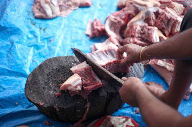 Kasap mezbahada bıçakla çiğ et kesiyor.