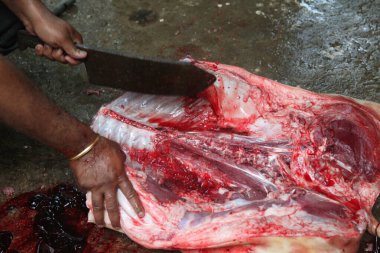 Kasap mezbahada bıçakla çiğ et kesiyor.
