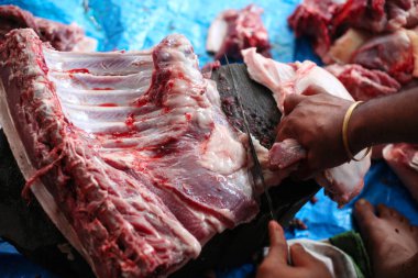 Kasap mezbahada bıçakla çiğ et kesiyor.