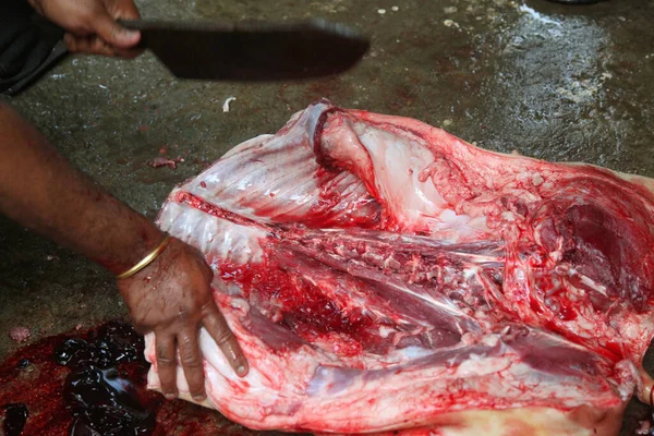 Kasap mezbahada bıçakla çiğ et kesiyor.