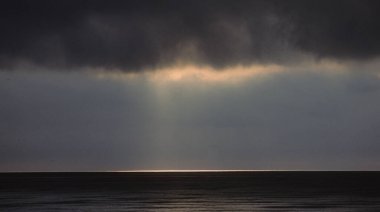 Adrian Denizi 'nde gün batımı kara bulutlar ve okyanusta muhteşem yansımalarla