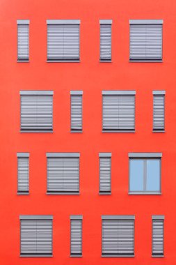 Kırmızı duvarda kepenk olan farklı boyutlardaki pencerelerin deseni
