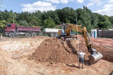 Fischbach, Almanya - 15 Temmuz 2020: büyük kazıcı bir aile evinin mahzeni için bir çukur kazıyor, işçiler kazı alanının uzaklığını ve yüksekliğini kontrol ediyor.