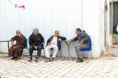 Houmt El Souk, Tunesya - 30 Nisan 2024: Arap erkekler Hawna 'daki eski örtülü suq' ın girişinde oturuyorlar..