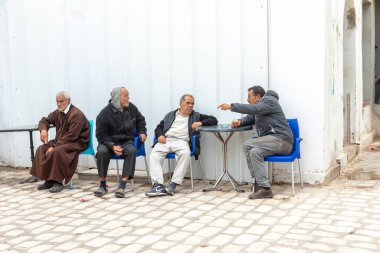 Houmt El Souk, Tunesya - 30 Nisan 2024: Arap erkekler Hawna 'daki eski örtülü suq' ın girişinde oturuyorlar..