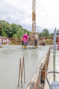 Fischbach, Almanya - 25 Ağustos 2020: inşaat alanında beton karıştırıcı ve darağacına sahip bir aile evinin temelini döken işçiler.