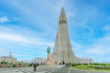 Reykjavik, İzlanda - 13 Temmuz 2023: Güzel Hallgrimskirkja kilisesi ve Reykjavik şehir merkezindeki kaşif heykeli. Gün batımında bulutlu gökyüzüne karşı en uzun katedralin önünde çimenler büyüyor..