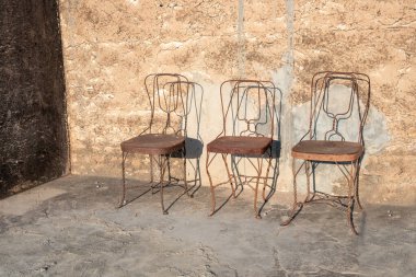 Hindistan 'da zamanın ve boşluğun sembolü olarak eski bir duvarın önünde duran üç eski paslı metal sandalye.