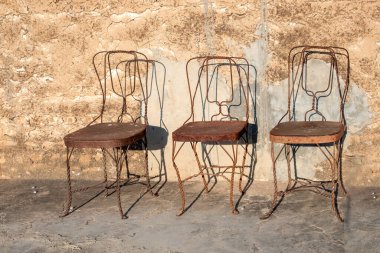 Hindistan 'da zamanın ve boşluğun sembolü olarak eski bir duvarın önünde duran üç eski paslı metal sandalye.