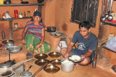 Pokhara, Nepal - 13 Ekim 2013: Tipik bir köy kulübesindeki adam ahşap kulübedeki toprak zeminde büyükannesiyle oturuyor. Pirinç içeride ahşap fırında pişirilir.