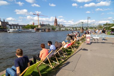 Frankfurt, Almanya - 9 Ağustos 2024: İnsanlar ana nehir ile Frankfurt 'un ufuk çizgisine bakan güverte sandalyesinin keyfini çıkarıyorlar..