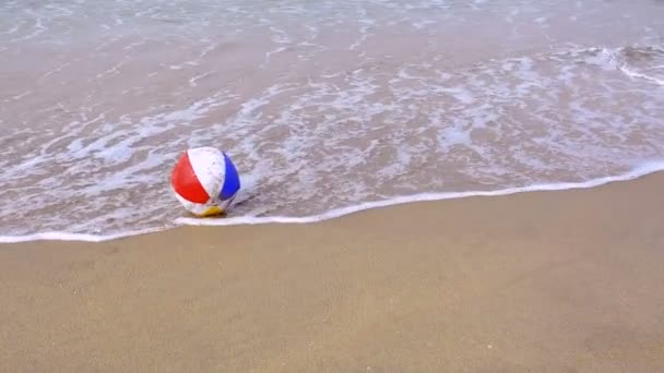 夏のカラフルなビーチボールは 穏やかで泡立つ波に押されながら砂のビーチまで洗い流されます — ストック動画