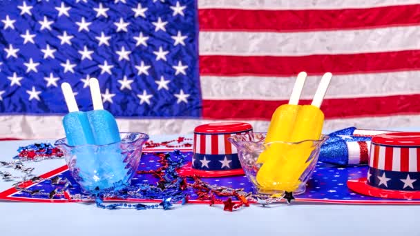 两个冰棒在清澈的杯子融化反对丰富多彩的美国爱国背景庆祝7月4日和阵亡将士纪念日 — 图库视频影像