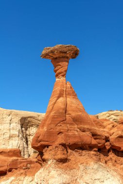 White and red sandstone toadstool hoodoo at Kanab Utah showing highly eroded spires and balanced harder rock on top framed by a blue sky. clipart