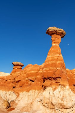 White and red sandstone toadstool hoodoo at Kanab Utah showing highly eroded spires and balanced harder rock on top framed by a blue sky. clipart