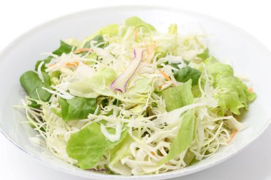 Beyaz arka planda öğütülmüş lahana ve marulu bir tabağa koy.  