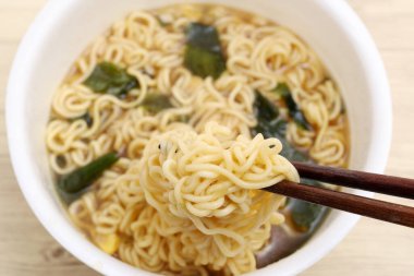 Boiled instant plastic cup noodles with chopsticks on table background