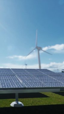 Göl ve şehir siluetine karşı yeşil enerji güneş panelleri ve rüzgar türbinleri, dikey video