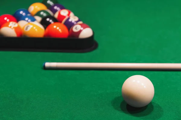 Colorful billiard balls with numbers with cue sticks and rack on green table.