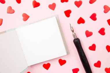 Mockup paper greeting card or wishes card on pink background. Pattern of red hearts, fountain pen for writing greeting and wishes, top view