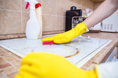 Man cleaning ceramic modern stove or hob with detergent agent. Hand in yellow gloves clean stove from burnt and grease dirt. Housework, professional cleaning service after tenants