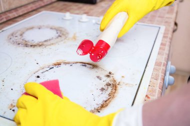 Man cleaning ceramic modern stove or hob with detergent agent. Hand in yellow gloves clean stove from burnt and grease dirt. Housework, professional cleaning service after tenants