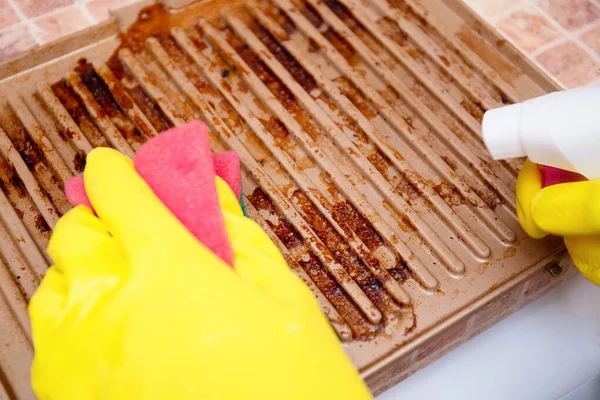 Man cleaning grilled pan or electric grill with detergent agent. Hands in yellow gloves clean grill burned and grease dirt after barbeque