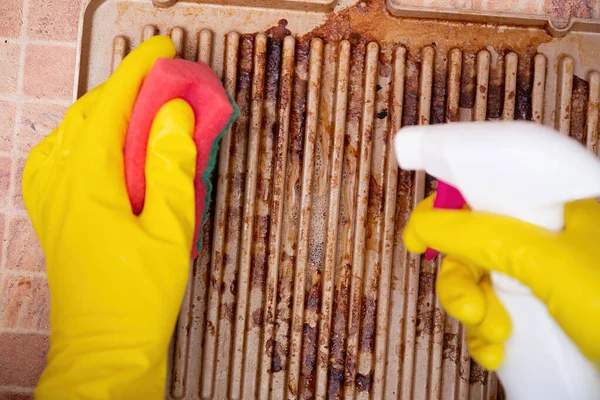 Man cleaning grilled pan or electric grill with detergent agent. Hands in yellow gloves clean grill burned and grease dirt after barbeque