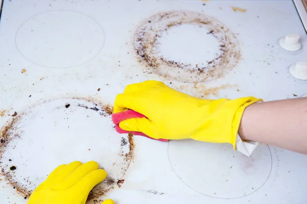 Man cleaning ceramic modern stove or hob with detergent agent. Hand in yellow gloves clean stove from burnt and grease dirt. Housework, professional cleaning service after tenants