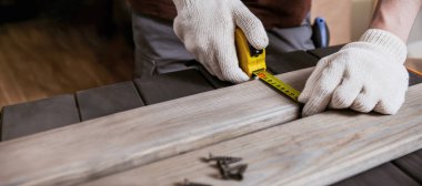 Tam ölçü. Eldivenli genç marangozun ahşap tahtada ölçümlerini sarı bant ile yaparken yaklaş..